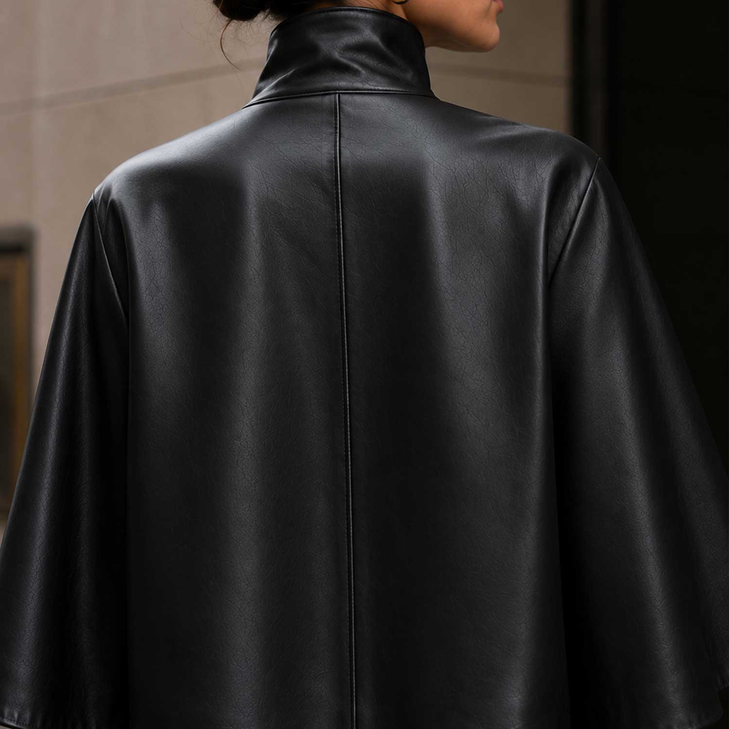 Front view of black sheepskin leather cape jacket with high-neck collar.
Side profile of genuine black leather cape with red satin lining.
Back view of handcrafted sheepskin leather cape jacket.
Close-up of high-neck snap-button collar on black leather cape.
Smooth premium sheepskin leather texture detail.
Luxury red satin lining inside black leather cape.
Flat-lay of black leather cape on a light marble table.
Women's luxury black leather cape in an editorial fashion photoshoot.