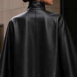 Front view of black sheepskin leather cape jacket with high-neck collar.
Side profile of genuine black leather cape with red satin lining.
Back view of handcrafted sheepskin leather cape jacket.
Close-up of high-neck snap-button collar on black leather cape.
Smooth premium sheepskin leather texture detail.
Luxury red satin lining inside black leather cape.
Flat-lay of black leather cape on a light marble table.
Women's luxury black leather cape in an editorial fashion photoshoot.