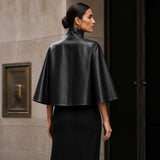 Front view of black sheepskin leather cape jacket with high-neck collar.
Side profile of genuine black leather cape with red satin lining.
Back view of handcrafted sheepskin leather cape jacket.
Close-up of high-neck snap-button collar on black leather cape.
Smooth premium sheepskin leather texture detail.
Luxury red satin lining inside black leather cape.
Flat-lay of black leather cape on a light marble table.
Women's luxury black leather cape in an editorial fashion photoshoot.