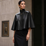 Front view of black sheepskin leather cape jacket with high-neck collar.
Side profile of genuine black leather cape with red satin lining.
Back view of handcrafted sheepskin leather cape jacket.
Close-up of high-neck snap-button collar on black leather cape.
Smooth premium sheepskin leather texture detail.
Luxury red satin lining inside black leather cape.
Flat-lay of black leather cape on a light marble table.
Women's luxury black leather cape in an editorial fashion photoshoot.