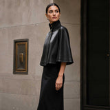 Front view of black sheepskin leather cape jacket with high-neck collar.
Side profile of genuine black leather cape with red satin lining.
Back view of handcrafted sheepskin leather cape jacket.
Close-up of high-neck snap-button collar on black leather cape.
Smooth premium sheepskin leather texture detail.
Luxury red satin lining inside black leather cape.
Flat-lay of black leather cape on a light marble table.
Women's luxury black leather cape in an editorial fashion photoshoot.